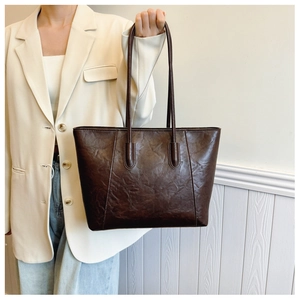 Detail view of deep brown faux leather tote bag with vintage texture on a model