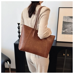 Brown faux leather tote bag held by a model in a minimalist home interior setting