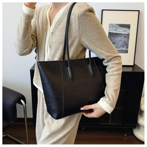 Close-up of a large black tote bag with leather texture worn over a model's shoulder