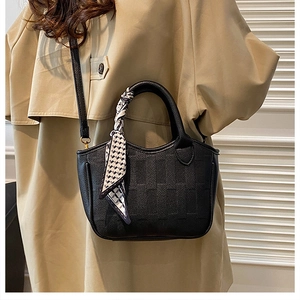 Close-up of black lychee leather bucket bag with silk scarf handle and trench coat styling