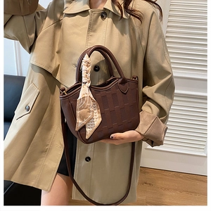 Detail of dark brown leather bucket bag with silk scarf on a trench coat model