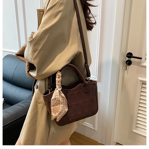 Detail of a dark brown bucket bag with woven texture and a silk scarf on the handle