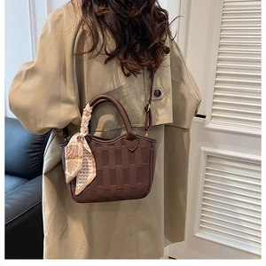 Detail of dark brown woven bucket bag with silk scarf on handle worn by model