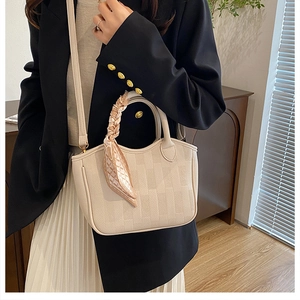 Detail of beige bucket bag with textured geometric pattern and silk scarf handle
