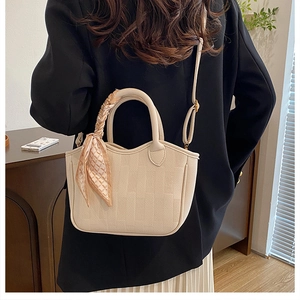 Detail of lychee textured leather bucket bag with decorative scarf handle and shoulder strap
