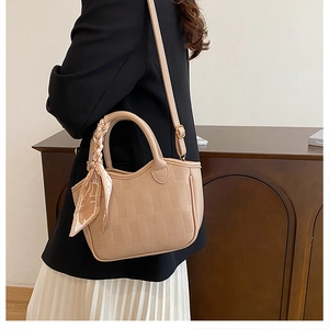 Close-up of beige leather bucket bag with silk scarf detail and adjustable shoulder strap