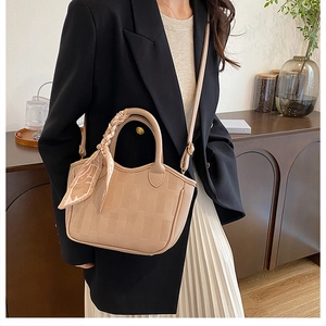 Detail of beige pebbled leather bucket bag with a decorative silk scarf and shoulder strap