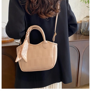 Detail of tan pebble leather bucket bag featuring a decorative floral silk scarf handle