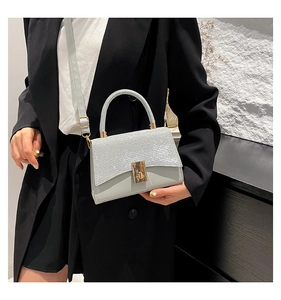 Detail view of light grey handbag showing glitter flap texture and gold twist lock clasp