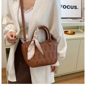 Brown textured bucket bag with silk scarf handle detail worn by a model in a cozy room