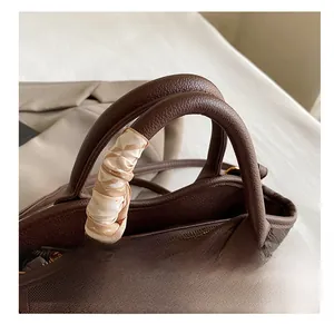 Detail of coffee brown bucket bag featuring a silk scarf wrapped handle and gold zipper