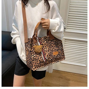 Leopard print canvas tote bag with plush bear charm and crossbody strap on casual outfit