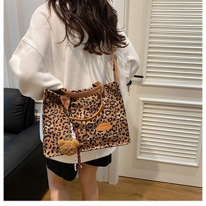 Detail of leopard print canvas tote bag featuring a brown leather logo and plush bear charm