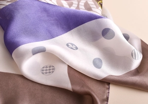 Gros plan du foulard en soie montrant des segments violets et blancs aux motifs de blasons