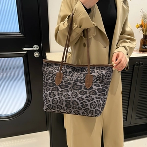 Large leopard print tote bag with brown leather handles worn with a beige coat