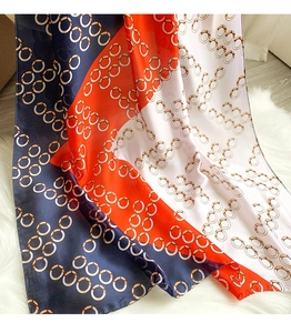 Detailed view of silk-like scarf with orange and blue chain patterns on white plush rug
