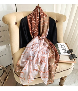 Detailed view of long satin scarf with brown chain prints draped on a beige sofa