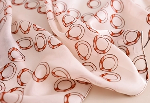 Detailed close-up of light pink silk-like scarf with reddish-brown ring patterns