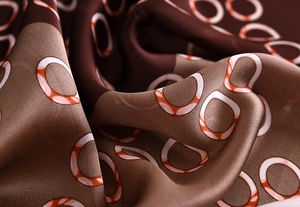 Macro detail of silky brown satin scarf with luxury chain pattern and soft folds