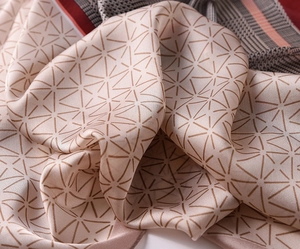 Detailed view of champagne pink silk scarf featuring geometric star patterns and satin gloss