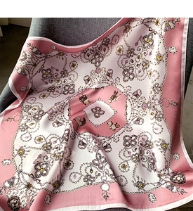 Détail d'un foulard en soie rose aux motifs bijoux, drapé sur un fauteuil en tissu gris