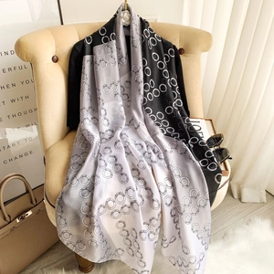 Faux silk scarf with black, white and grey chain patterns draped on a cozy sofa