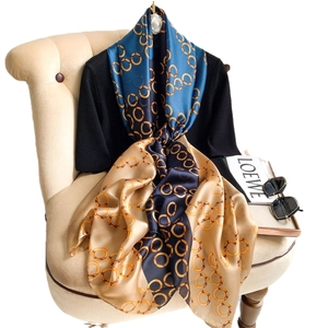 Faux silk scarf with navy and gold chain print draped over a black top and chair