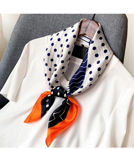 Détail d'un foulard en soie à pois marine avec une bordure orange vif sur un cintre