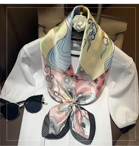 Detailed close-up of a floral silk scarf featuring a pearl buckle on white knitwear