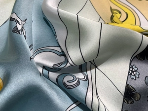 Detailed close-up of blue and yellow printed silk scarf with floral bird patterns