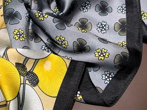 Detailed view of silk-like scarf with floral and abstract geometric patterns in grey and yellow