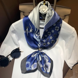 Detail of silk scarf with crane cloud print and gold ring buckle on beige leather bag