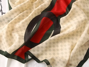 Macro detail of luxury silk scarf showing beige monogram print and red-green stripe