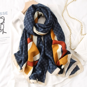 Detail of navy blue and orange silk shawl with monogram pattern on wooden hanger