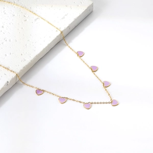 Detailed shot of golden chain necklace with seven purple heart pendants on white marble