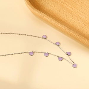 Silver chain necklace with purple heart pendants on a soft beige background