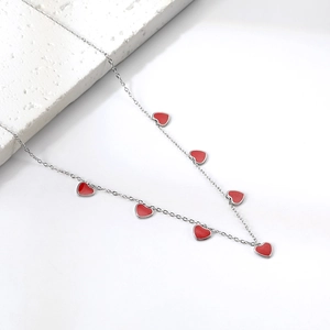 Detail view of a thin chain necklace with seven red enamel heart charms on a white stone