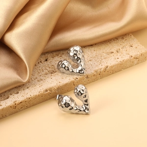 Polished silver heart stud earrings with hammered texture on a travertine stone base