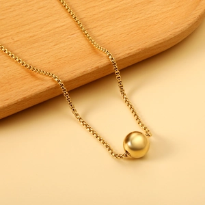 Détail d'un pendentif boule dorée minimaliste sur une chaîne fine au fini métallique poli