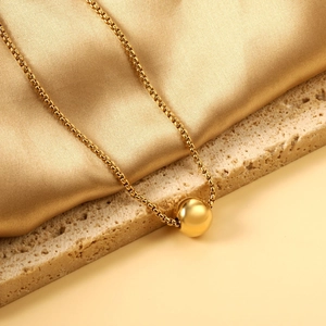 Collier à pendentif boule dorée minimaliste sur fond élégant en satin et pierre