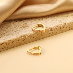 Detailed view of gold heart huggie earrings with pink crystals on a satin background
