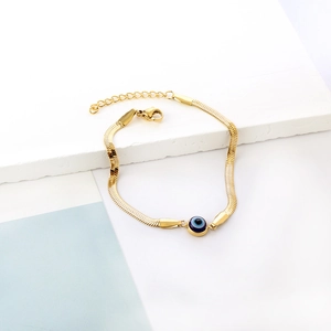 Detail of gold snake chain bracelet with evil eye charm on white stone backdrop
