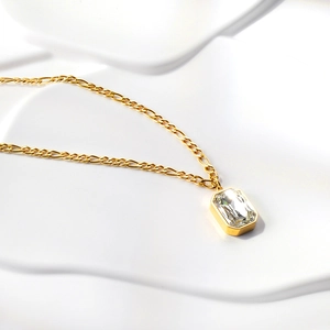 Macro shot of gold Figaro chain necklace featuring a rectangular emerald-cut crystal pendant