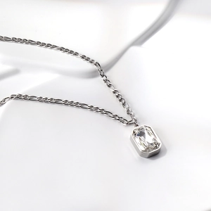 Macro view of silver Figaro chain and clear rectangle gemstone pendant on white surface