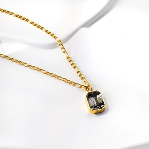 Close-up of gold Figaro chain with rectangle dark grey gemstone pendant on white background