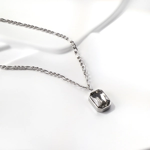 Detailed close-up of a silver Figaro chain necklace with a smoky grey rectangle crystal