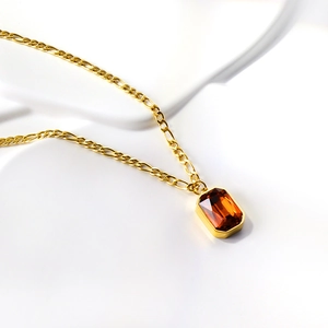 Macro detail of vintage gold Figaro chain necklace featuring amber rectangle gemstone pendant