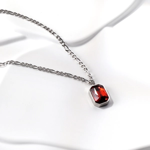 Macro shot of rectangular red gemstone pendant on silver Figaro chain with white background