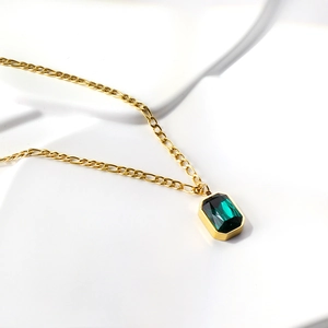 Macro view of gold Figaro chain necklace featuring a rectangular emerald gemstone pendant