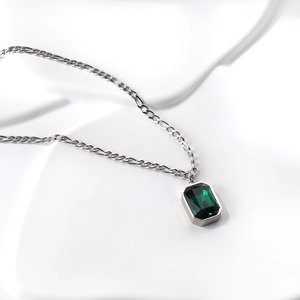 Macro view of emerald-cut green crystal pendant on silver Figaro chain necklace